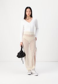 Hvit, ribbestrikket knappelin cardigan, kremfarget strikket maxiskjørt med diagonale mønstre, svart blomstertrukket snorlås-sekk, og hvite sneakers.