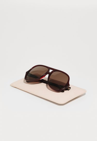 Brown-tinted sunglasses with a deep burgundy plastic frame, resting on a light pink textured case.