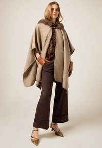 Beige ullkappa med en pälskrage, bärs över en brun leopardmönstrad topp. Kombinerad med bruna byxor och klackar med ormmönster.