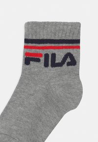 Calzino grigio con strisce blu navy e rosse vicino alla parte superiore. Il marchio "FILA" è ben visibile in blu navy sul lato. Materiale a maglia testurizzata.