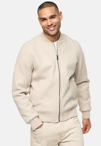 Beige bomber jacket made of soft fabric, featuring a front zipper, ribbed cuffs, and side pockets. Smooth texture with a casual design.