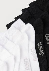 Βαμβακερές κάλτσες σε λευκό και μαύρο χρώμα, με ριγωτή υφή. Κάθε ζευγάρι έχει διακριτικά λογότυπα σε αντίθετο χρώμα. Πέντε ζευγάρια στοιβαγμένα.