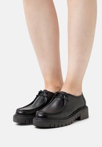 Zwarte leren schoenen met een gestructureerde afwerking, ronde neus en een robuuste zool; voorzien van decoratieve veters en een lage snit.