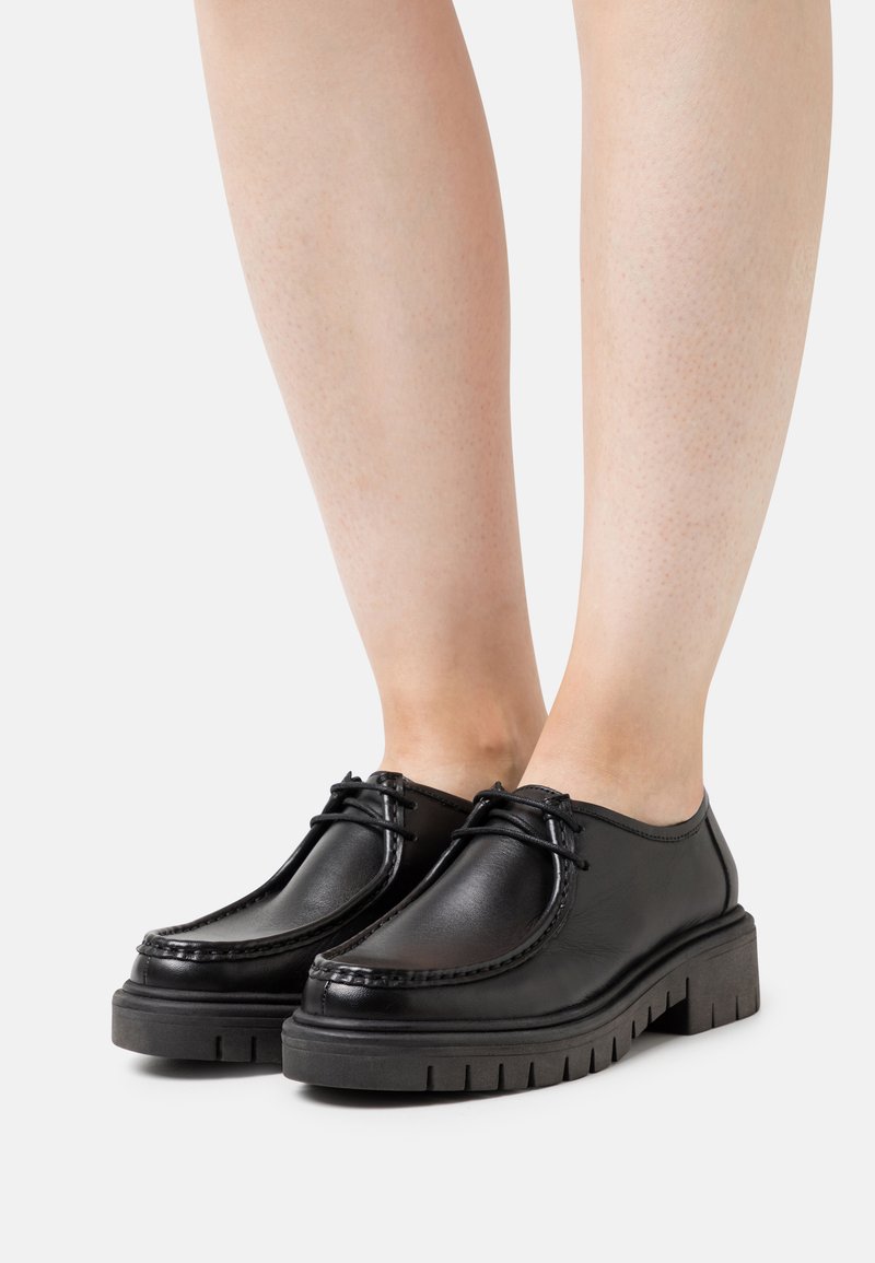 Zwarte leren schoenen met een gestructureerde afwerking, ronde neus en een robuuste zool; voorzien van decoratieve veters en een lage snit.