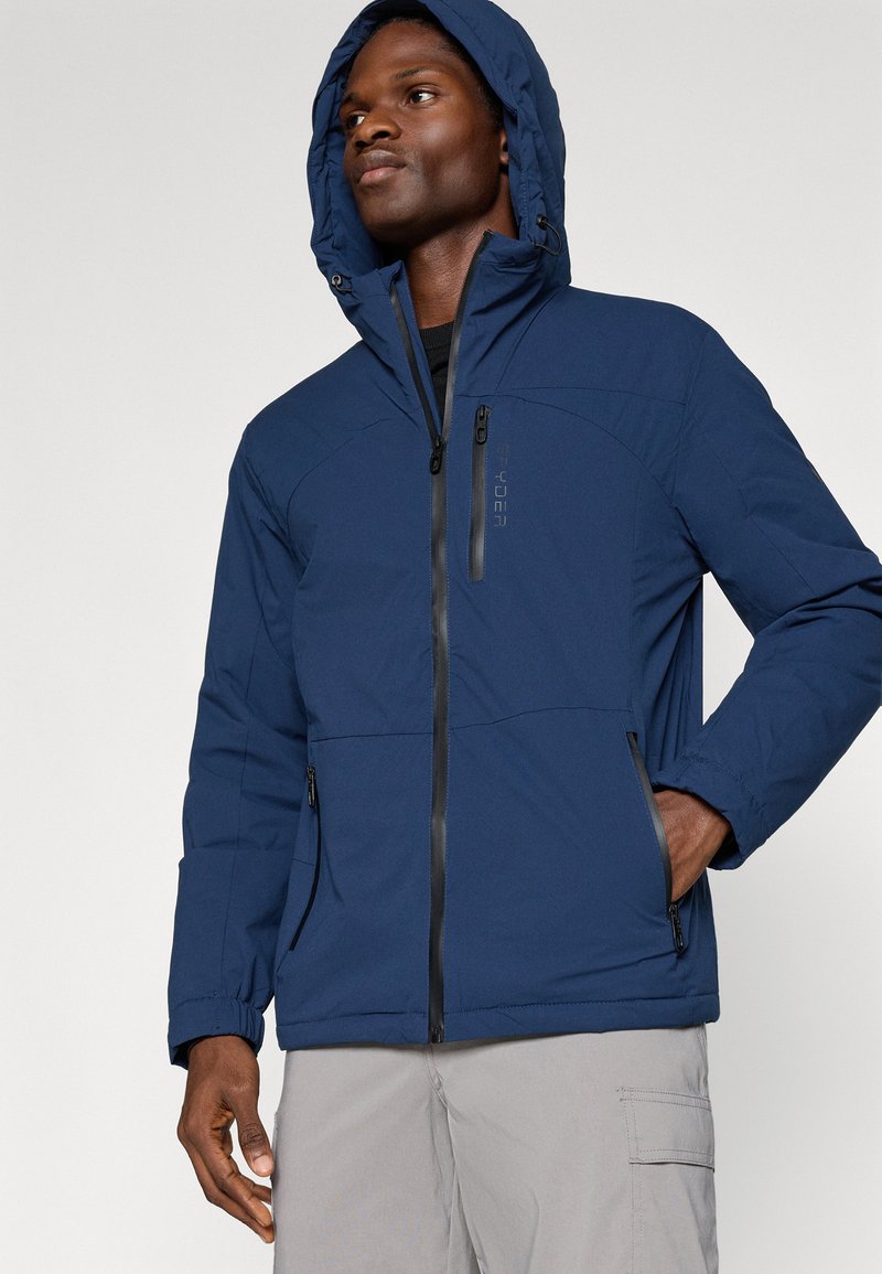 Chaqueta acolchada azul marino con capucha, que cuenta con un cierre frontal y dos bolsillos laterales. Fabricada en un tejido texturizado con cremalleras negras en contraste.