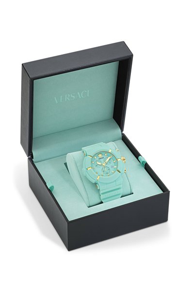 Orologio Versace con cinturino in silicone turchese chiaro e quadrante abbinato, con dettagli dorati, esposto in una scatola nera con interiora menta.