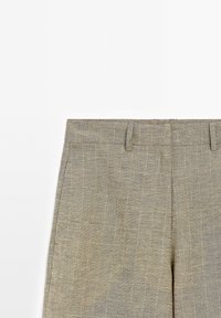 Pantalon en lin beige avec passants de ceinture, poches latérales et un motif texturé subtil sur fond blanc.