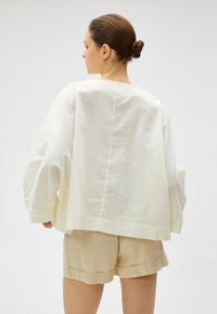 Lysfarvet linnedragt med overdimensionerede ærmer og lige snit, parret med matchende shorts. Blød tekstur og minimalistisk design.