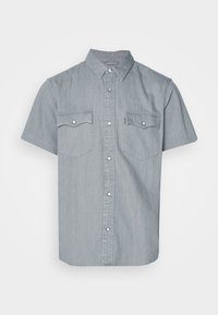 Camisa de mezclilla de manga corta en azul claro, con cuello abotonado, dos bolsillos en el pecho y detalles en hardware plateado. Textura suave.