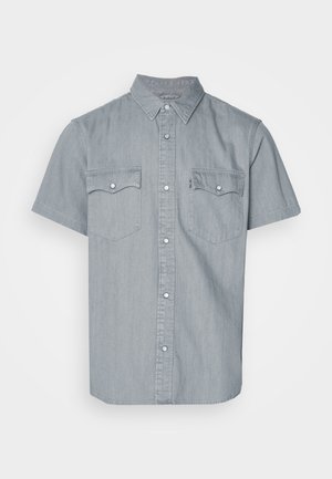 Chemise en denim à manches courtes de couleur bleu clair, avec un col boutonné, deux poches poitrine et des accents en métal argenté. Texture lisse.