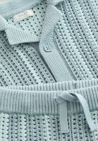 Pull en maille bleue avec un design texturé. Comprend une patte de boutonnage et un ourlet côtelé. Material léger et respirant.