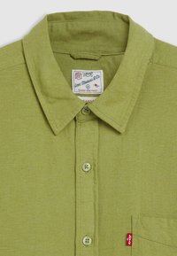 Camicia botton-down verde chiaro realizzata in tessuto testurizzato, con colletto sovrapposto, taschino sul petto e etichetta con marchio con accentuazione rossa.