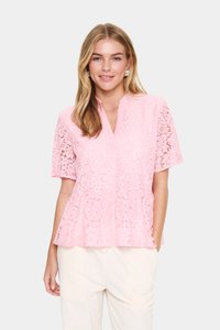 Blouse en dentelle rose à manches courtes, avec un col en V et un design peplum, mettant en valeur des motifs floraux et un tissu texturé.