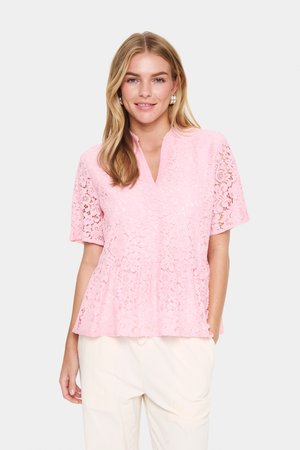 Lyserød bluse i blonder med korte ærmer, der har en v-hals og peplum-design, prydet med blomstermønstre og et struktureret stof.