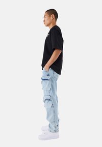 Camiseta negra de cuello redondo, jeans cargo azul claro con múltiples bolsillos y zapatillas blancas. Diseño minimalista, corte casual y textura suave.