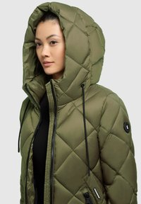 Mikserani maslinasto zelena puffer jakna s velikom kapuljačom, crnim vezicama, džepovima na patentni zatvarač i crnim akcentom na lijevom ramenu.