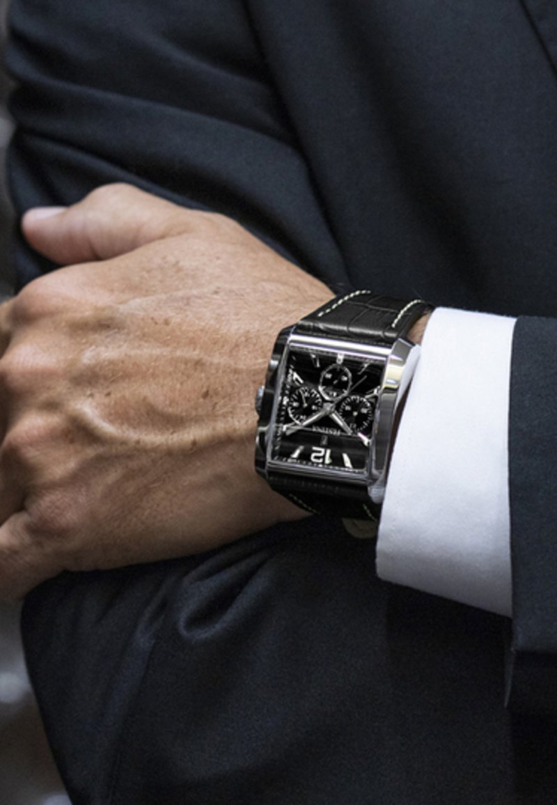 Orologio rettangolare nero con cinturino in pelle, dettagli in argento e un quadrante nero con più sottodial e un display della data a ore 12.