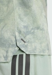 Jasnozielona koszulka sportowa z teksturowanym wzorem, rozcięciami na hemie oraz czarnymi poziomymi paskami na pasujących szortach.