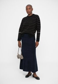 Suéter a rayas negro y marrón, falda larga de punto azul, bailarinas negras y un pequeño bolso beige. Diseño simple y texturizado, silueta ajustada.