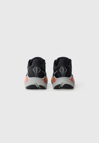 Pantofi sport negri cu un superior din țesătură texturată, având o talpă intermediară gri și accente colorate în roșu și galben pe talpă.