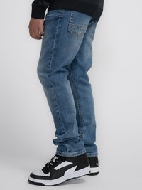 Jeans de mezclilla azul oscuro con corte recto, presentando un desvanecimiento sutil. Combinados con zapatillas negras y blancas, que muestran un diseño atlético clásico.