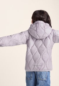 Light lavender puffer jacket with a quilted wave pattern, hood, and reflective accent. Paired with blue denim jeans.