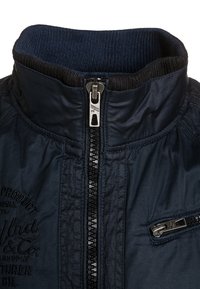 Navy blue jacket collar with black ribbed inner lining, central zipper, small zipped pocket on right, and embroidered text on left side.