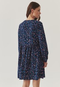 Marine jurk met lange mouwen, voorzien van een bloemenpatroon in roze en blauw. De gathered taille en de uitlopende rok creëren een ontspannen silhouet.