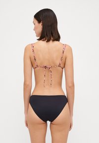 Black bikini bottom paired with a multi-colored floral print top, featuring thin adjustable straps and a bow tie closure at the back.