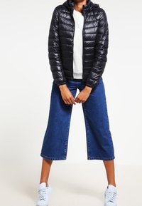 Sort pufferjakke med hætte, quiltet design og lange ærmer, kombineret med blå denim culottes med vide ben og hvide sneakers.