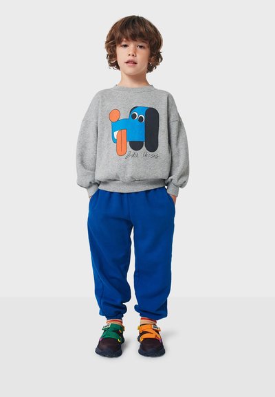 Grå sweatshirt med grafisk design som har blå och orange former. Blå sweatpants och mångfärgade sneakers med strappar fulländar outfiten.