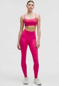 Rosa athletisches Cropped-Top und hochgeschnittene Leggings; glattes, elastisches Material; minimalistisches Design; kombiniert mit weißen Turnschuhen.