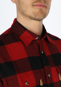 Rood en zwart geruit overhemd van een wolmix stof, met een puntige kraag, knoopsluiting en twee borstzakken met flaps.