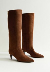 Stivali al ginocchio in suede marrone con punta appuntita e tacco basso, caratterizzati da un design senza cuciture e una texture liscia.