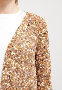 Texturovaný cardigan v hnědých tónech se žlutými a bílými skvrnami. Design s otevřeným předním dílem, který obsahuje jemný vzor stehu a měkký materiál.