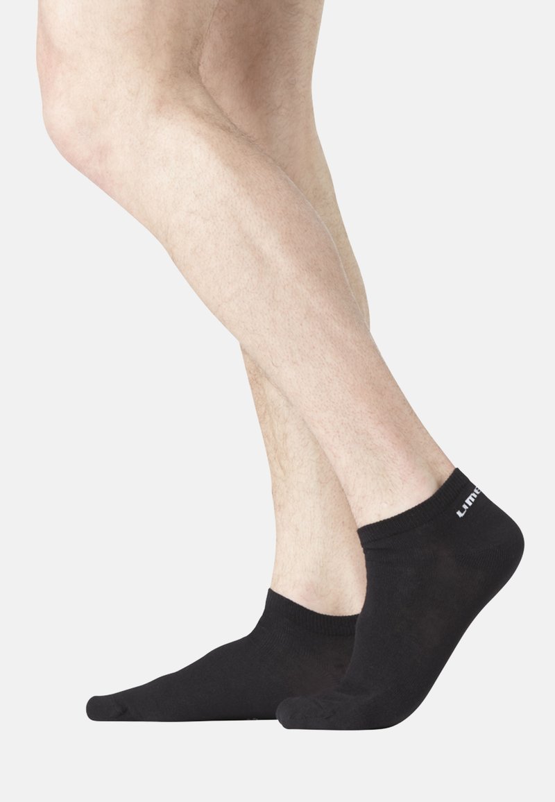 Chaussettes noires à chevilles en matériau doux avec un bord côtelé, affichant un branding minimaliste blanc à l'arrière.