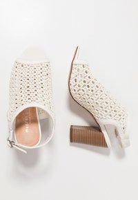 Bílé lodičky s otevřenou špičkou, které mají pletený svršek, hladké kožené detaily a texturovaný hnědý blokový podpatek. Zapínání na zip na boku.