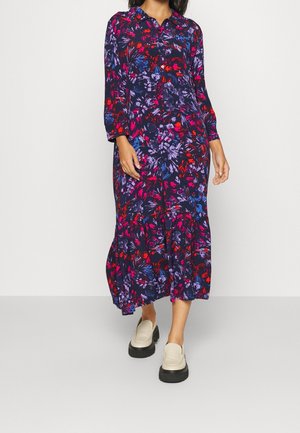 Femme portant une robe midi à manches longues boutonnée avec un motif floral abstrait coloré, associée à des mocassins à plateforme beige.