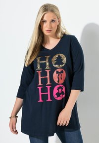 Mörkblå V-halsad skjorta med ¾ ärmar, med dekorativ "HO HO HO" i guld och rosa glitter, inklusive en björngrafik. Mjuk tyg.