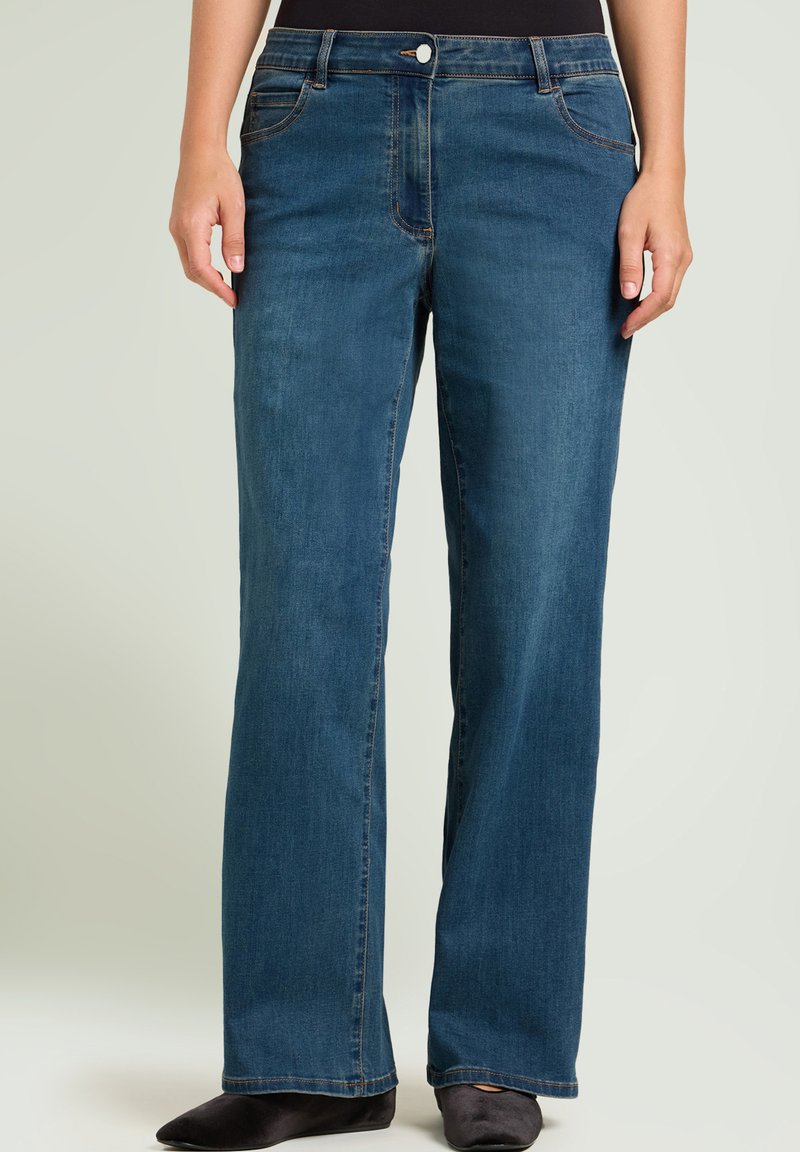 Pantalones de mezclilla de pierna ancha en un lavado azul oscuro, con cierre de botones, trabillas para cinturón y bolsillos delanteros. Textura lisa con costuras en contraste.