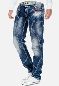 Jeans in denim blu con una finitura usurata. Presentano cuciture bianche a contrasto e un'originale dettagliatura delle cuciture. Abbinati a sneakers bianche.