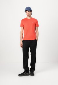 Tricou scurt roșu cu mâneci scurte și logo. Pantaloni negri croiți. Adidași negri cu accente albe. Capac albastru. Ținută simplă și casual.