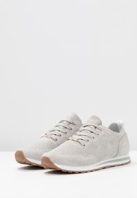 Chaussures de sport gris clair en daim avec motifs perforés, semelle intermédiaire blanche et semelle extérieure en caoutchouc marron. Dotées d'une fermeture à lacets et d'un logo.