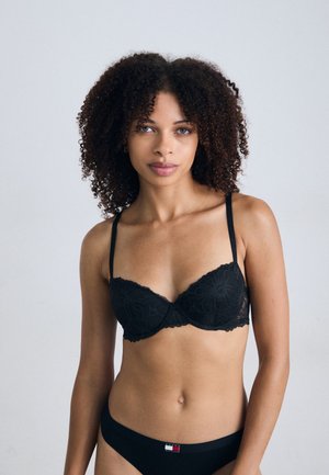 Black lace bra with underwire and adjustable straps, featuring floral patterns and scalloped edges; paired with black low-rise briefs.