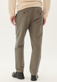 Pantaloni bărbați de culoare verde măslin, cu o croială slim, care prezintă un material texturat, buzunare la spate cu nasturi și detalii cu elastic la talie.