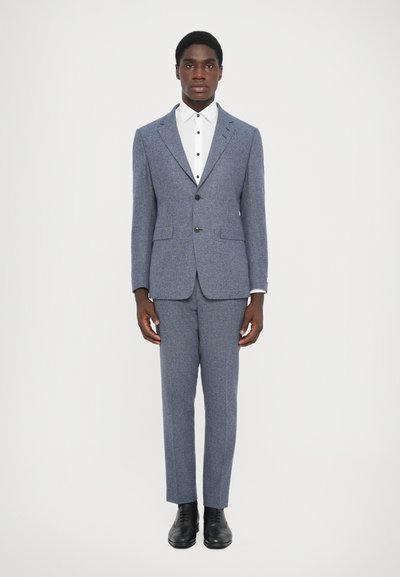 Costume texturé gris avec une veste ajustée et un pantalon assorti. Chemise blanche avec col boutonné. Des chaussures habillées noires complètent la tenue.