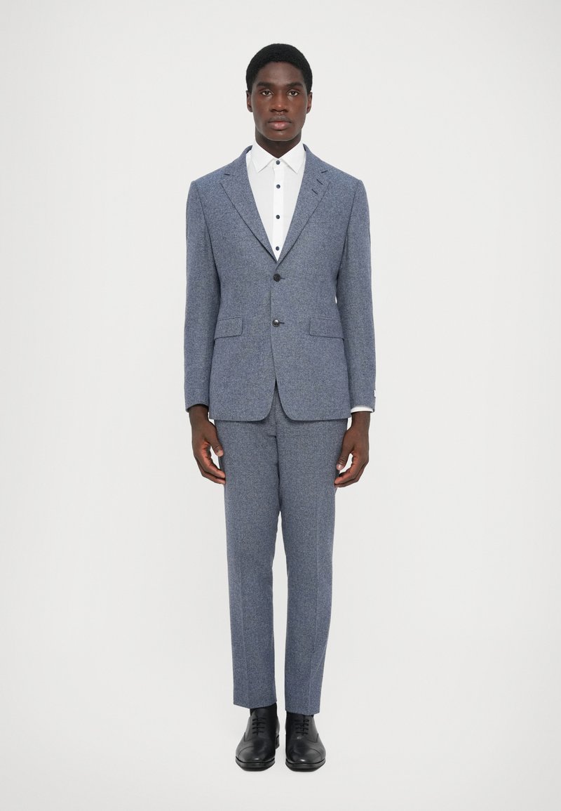 Blue herringbone suit jacket and trousers with a white dress shirt featuring black buttons, completed with black dress shoes.