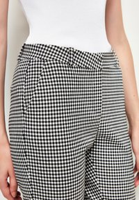 Pantalon à motif vichy noir et blanc avec une coupe ajustée, doté de poches latérales et d'une taille plate pour un look structuré.
