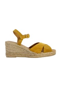 Wedge sandal in mustard yellow suede, featuring an ankle strap with a buckle and a braided jute wedge heel. Open-toe design with crossed straps.