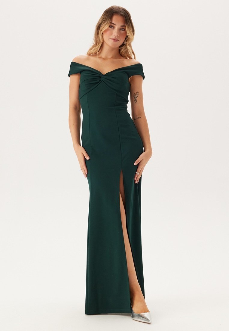 Robe émeraude décolletée avec un détail de nœud torsadé au niveau de la poitrine et une fente haute sur la cuisse. Tissu lisse et silhouette ajustée.